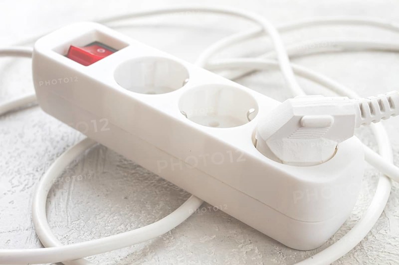 Power strip with multiple sockets and a switch in a cluttered setup on a textured surface during daytime