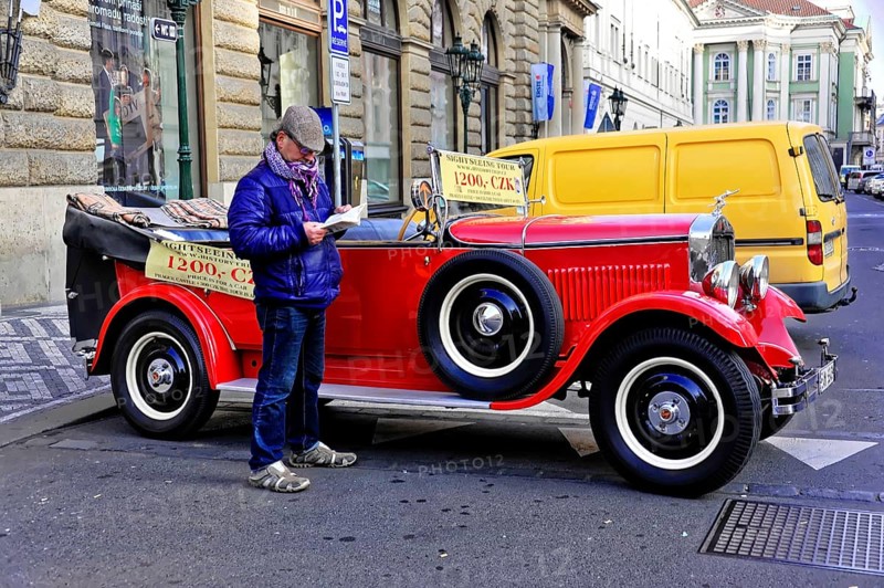 Prague, Czech Republic, Europe, Man reading in front of a classic red vintage car on a busy street in Prague
