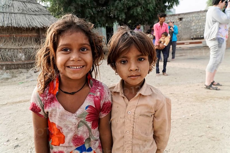 Sawai Madhopur, Kota, Rajasthan, North India, Asia, Two children smiling friendly, a village in the background. Girl in colourful and beige clothes, India