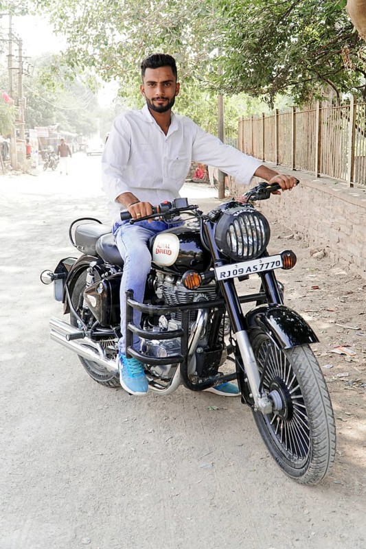 Kota, Rajasthan, North India, Asia, Man sitting on a black Royal Enfield motorbike on a dusty road, India
