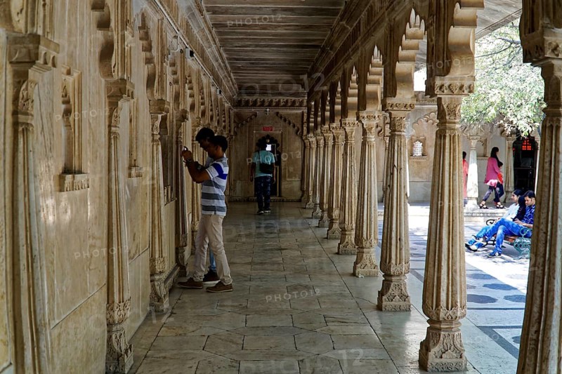 City Palace, Udaipur, Rajasthan, India, Asia, A long corridor decorated with stone carvings and people in a historic Indian building, North India