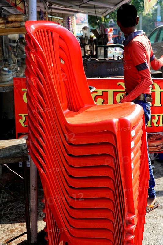 Udaipur, Rajasthan, North India, India, Asia, Stacked red plastic chairs in a lively market with people walking around