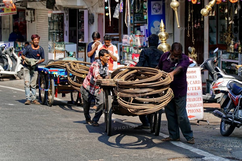 Udaipur, Rajasthan, North India, Asia, Several men pulling wooden carts with rolled up ropes on a busy street