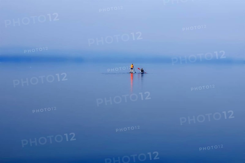 A calm lake (Steinhuder Meer) with paddleboarders under a blue and wide sky, Wunstorf