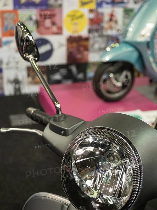 Retro scooter mirror in front of a blurred background with posters and another scooter, dortmund, deutchland