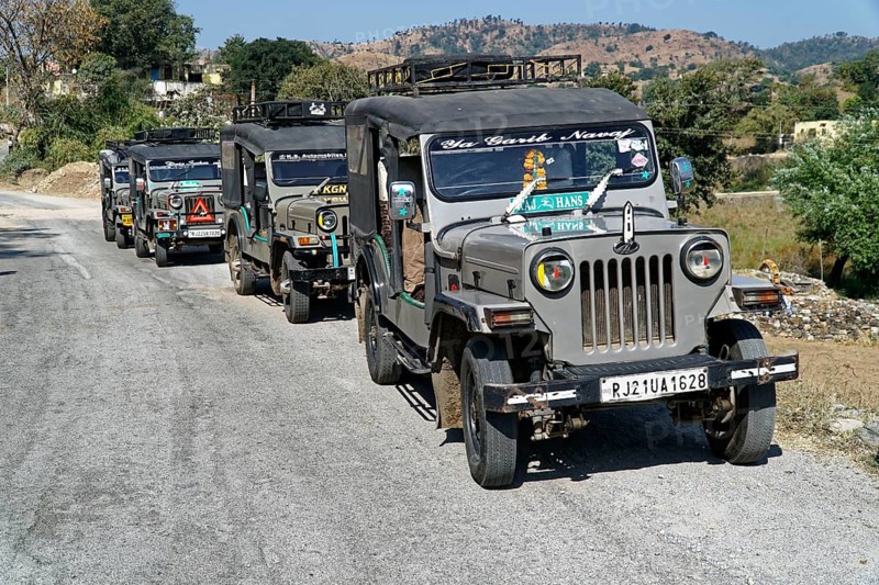 A convoy of jeeps drives along a country road in a mountainous region, Ranakpur, Jodhpur, Rajasthan, North India