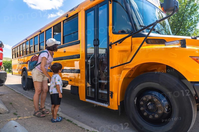 Caring mother supports her son as he prepares to board the school bus for his first day back to school, marking a significant milestone in his education