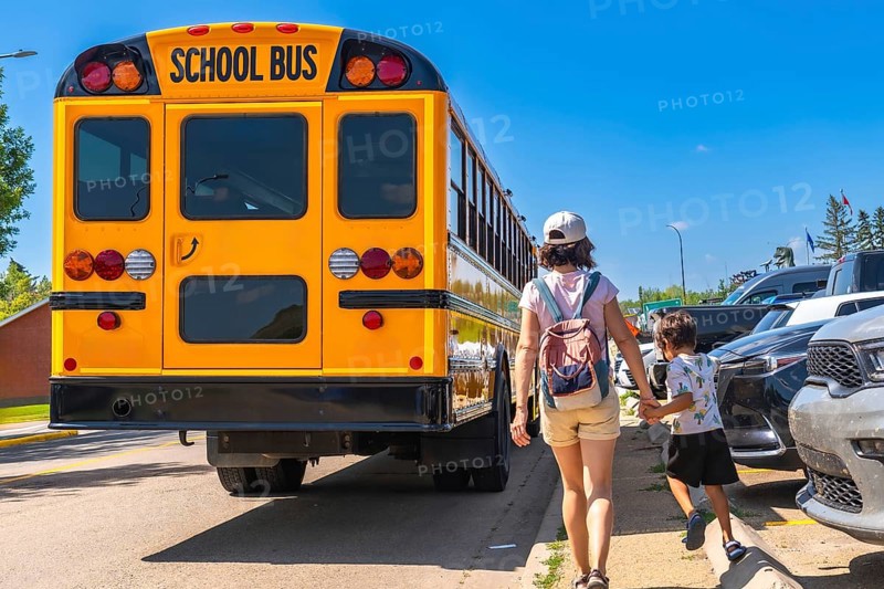 Mother holding son's hand walking towards a school bus on the first day back to school, representing the start of a new academic year and childhood education