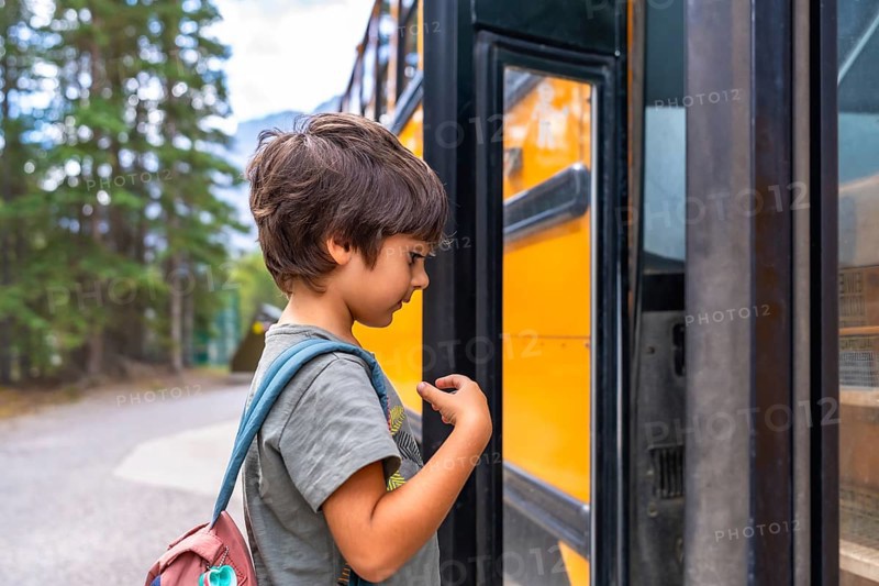 Curious preschool student with a backpack examines a yellow school bus before boarding, showing the anticipation and excitement of going back to school