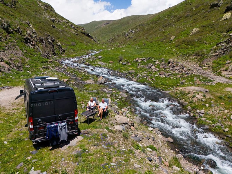 A campervan stands next to a river in the mountains where people sit at a table and enjoy nature, aerial view, campervan, camper, Arkashian River, Aragazotn Province, Armenia