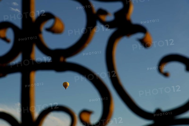 Yellow hot air balloon flying against a blue sky, seen through an ornate metal gate in ronda, malaga, spain