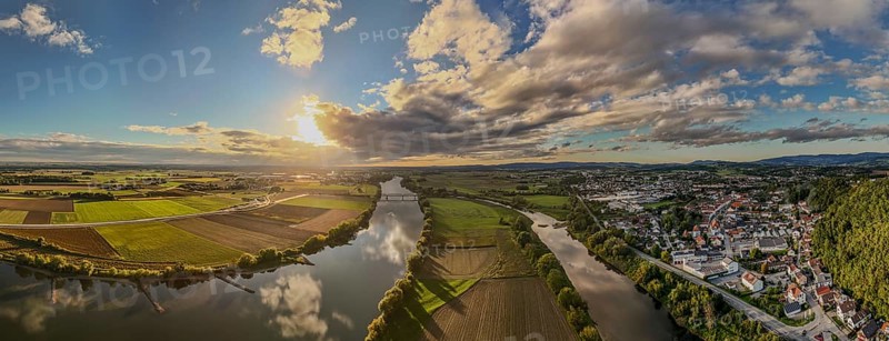 The sunset bathes the river landscape of the Danube in a warm light. A few fields and meadows border the calm water. The sky is partly cloudy and radiates a peaceful atmosphere. Bogen, Lower Bavaria