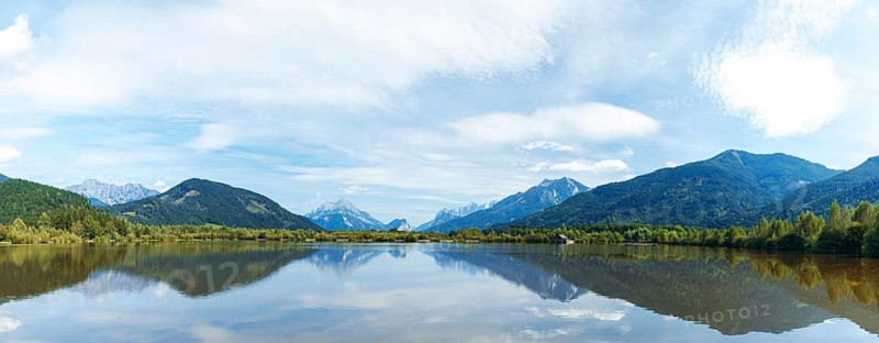 Panoramic lake reflects the surrounding mountains and the slightly cloudy sky, Admont, Styria, Austria