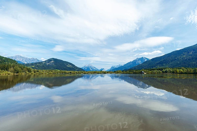 Panoramic lake reflects the surrounding mountains and the slightly cloudy sky, Admont, Styria, Austria