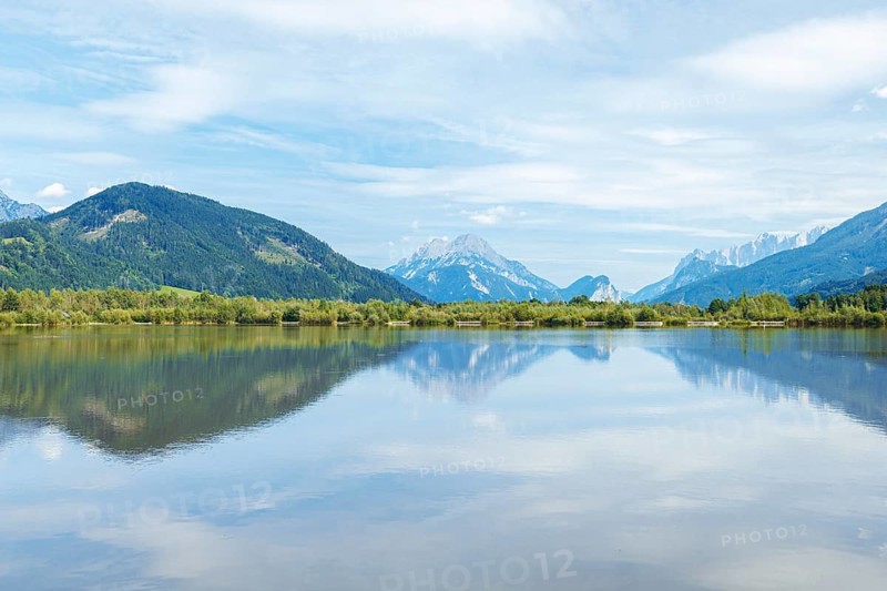 Panoramic lake reflects the surrounding mountains and the slightly cloudy sky, Admont, Styria, Austria