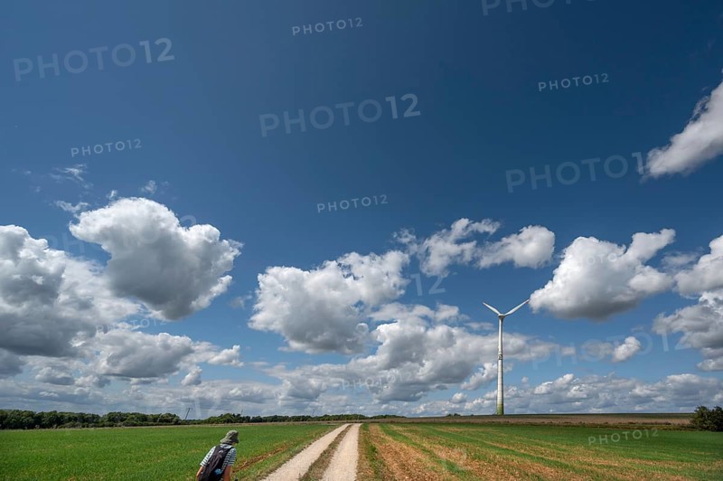 Hiker on a country lane in Franconian landscape, a windmill behind, cloudy sky, Karsberg, Upper Franconia, Bavaria, Germany