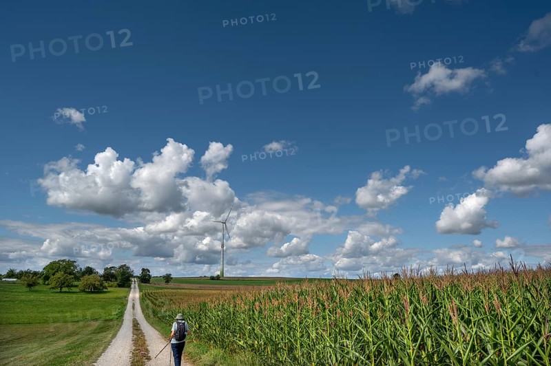 Hiker on a country lane in Franconian landscape, a windmill behind, cloudy sky, Karsberg, Upper Franconia, Bavaria, Germany