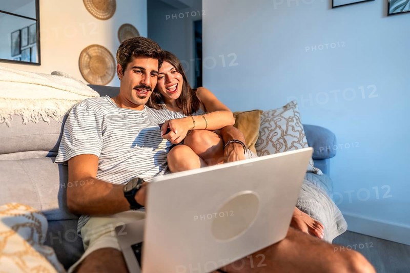 Young couple enjoying a movie on their laptop, laughing and having a good time together on the sofa in their living room