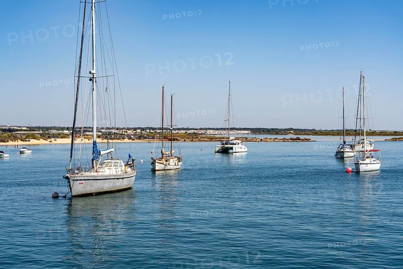 Sailboats anchored in the Gilão River, in front of the beach Praia da Ilha de Tavira, on the island off Tavira, Algarve, Portugal