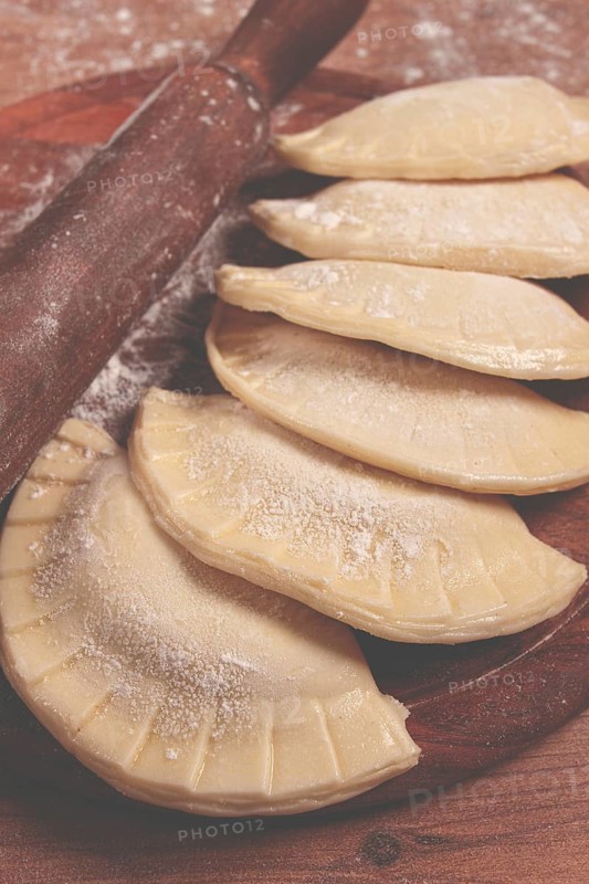 Raw chebureks, mini, on a cutting board, wooden table, close-up, no people
