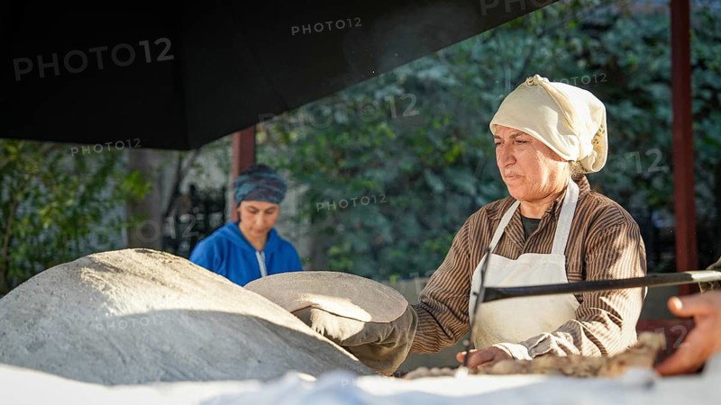 A Turkish woman bakes traditional bread on a clay tandoor oven in a rural village, Hatay, Hatay, Türkiye