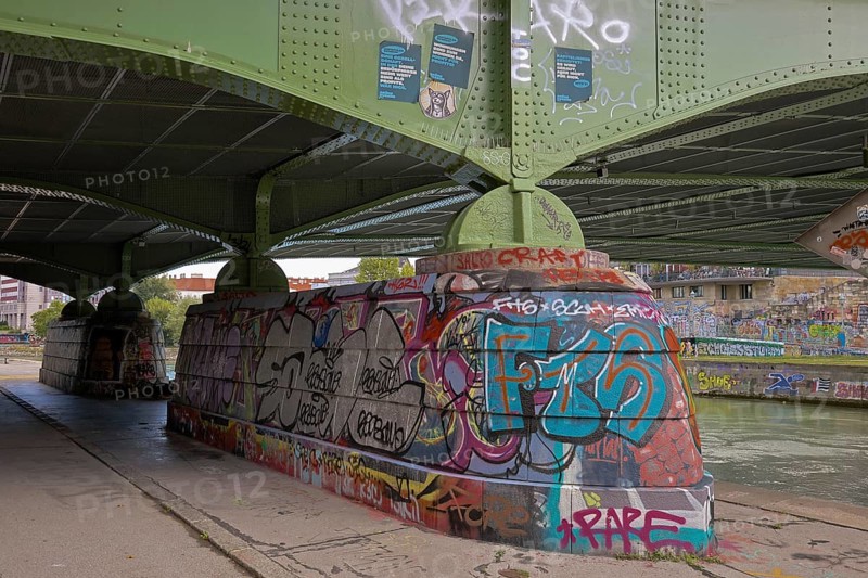 Under a bridge with graffiti on the retaining walls and a river in the background, Am Donaukanal Innere Stadt Vienna Austria