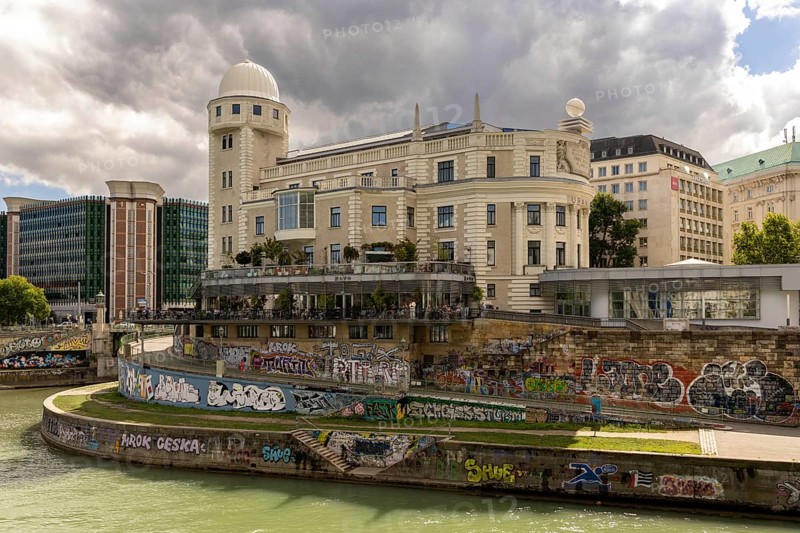 A historic building on the riverbank with graffiti on the wall and a cloudy sky Urania Ringstraße Vienna Austria
