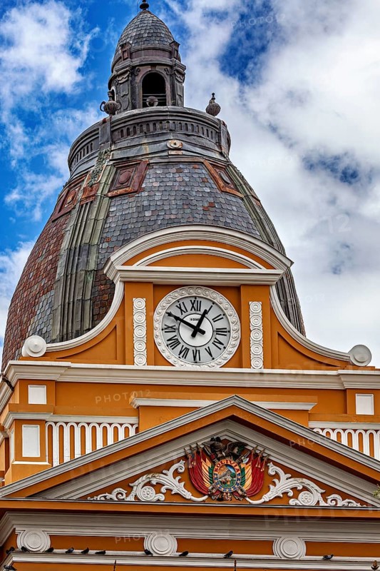 Architecturally richly decorated tower with clock and coat of arms under a cloudy sky, The Presidential Palace of La Paz in Bolivia
