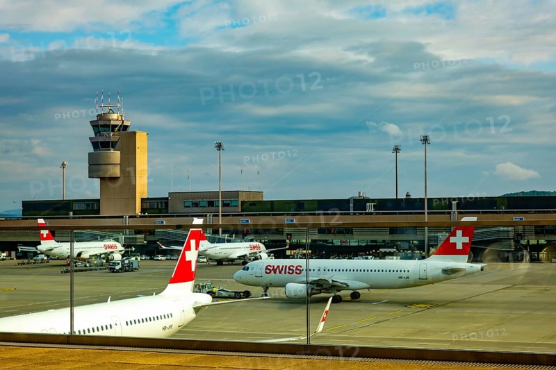 Swiss Airlines Passenger Airplane and Air Traffic Control Tower on the Airfield in a Sunny Summer Day with Blue Sky and Clouds From the Airport in Kloten, Zurich, Zurich Canton, Switzerland