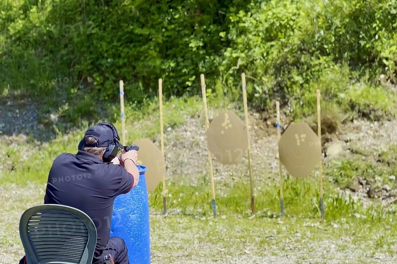 Man Sitting on a Chair and with Handgun and Holster Sport Training IPSC Shooting on an Outdoor Shooting Range with Target in a Sunny Day in Italy