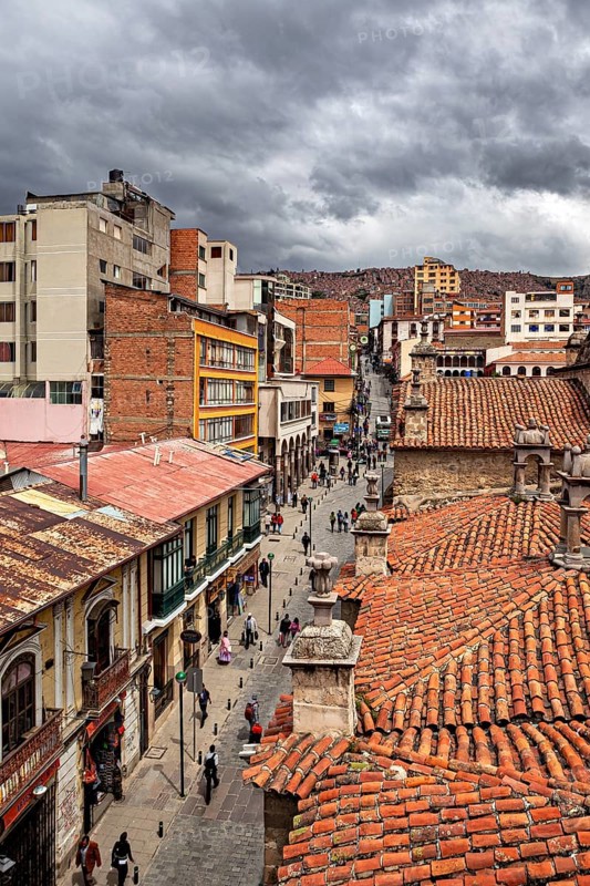 Historic city view with red tiled roofs under a cloudy sky, people in the streets of La Paz in Bolivia