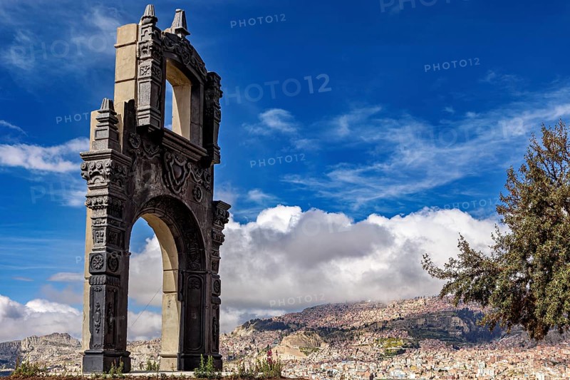 A stone gate with ornate decorations in front of a sprawling cityscape and a blue sky, The gate at the Killi Killi viewpoint in La Paz, Bolivia