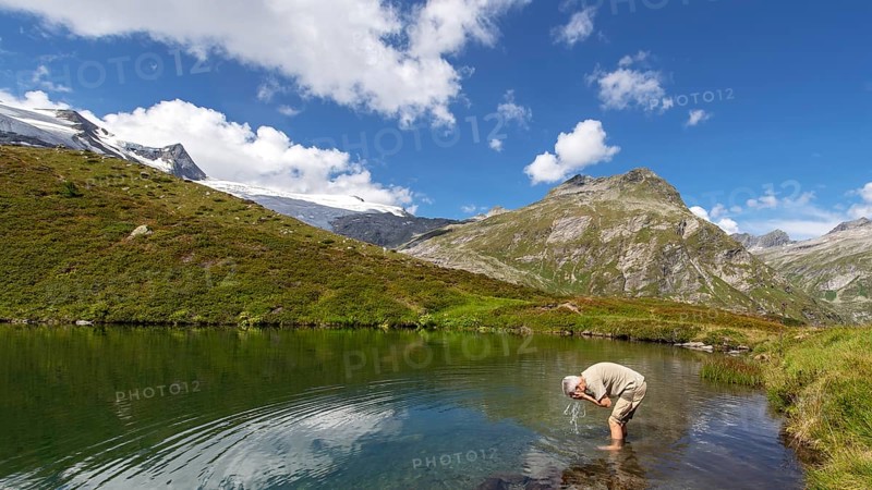 Hiker refreshes himself in the Salzbodensee lake on the glacier show trail in the Tauerntal valley, Hohe Tauern National Park, East Tyrol, Austria