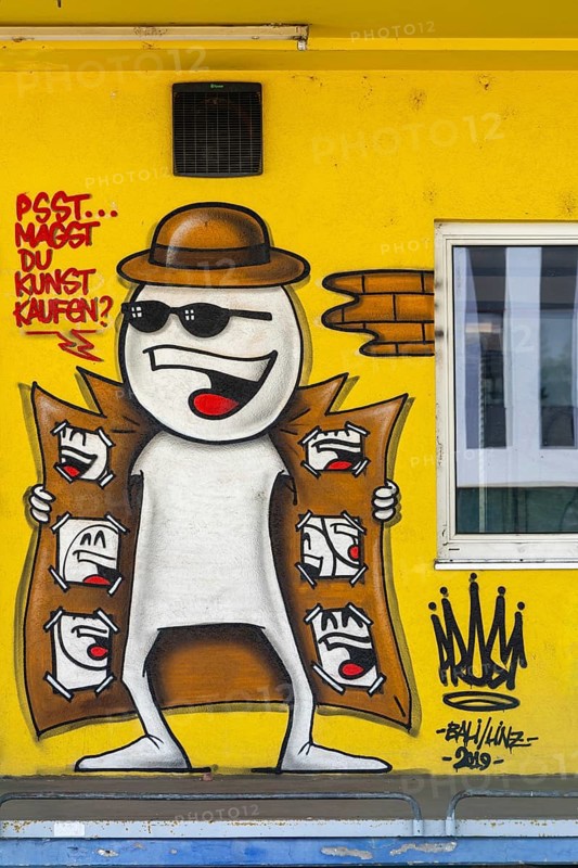 Funny comic-style graffiti with a figure in a trench coat on a yellow wall, at the harbour in Linz, Upper Austria Austria
