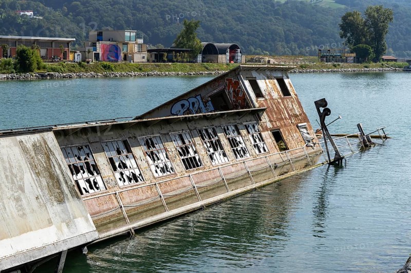 Partially submerged ship with graffiti near shore with mountains, at the harbour Linz Upper Austria Austria