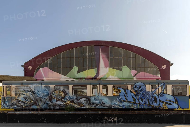 Skeleton graffiti on a train in front of a large building with a colourful facade, at the port of Linz Upper Austria Austria
