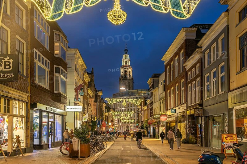 Shopping street Oosterstraat and the church tower Martinitoren or Martinitower of the Martinikerk or Martinikirche at dusk, Groningen, Netherlands