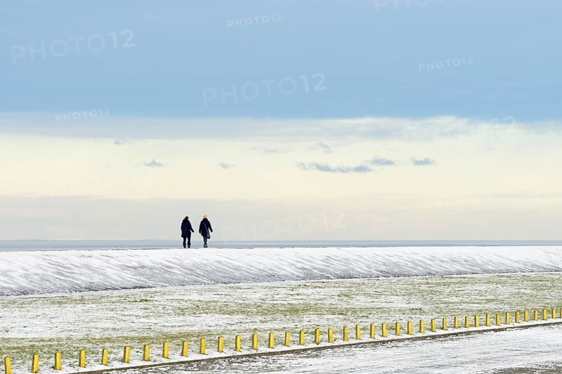 North Sea coast on a winter's day, people walking over a snow-covered dyke, Norddeich, Lower Saxony, Germany