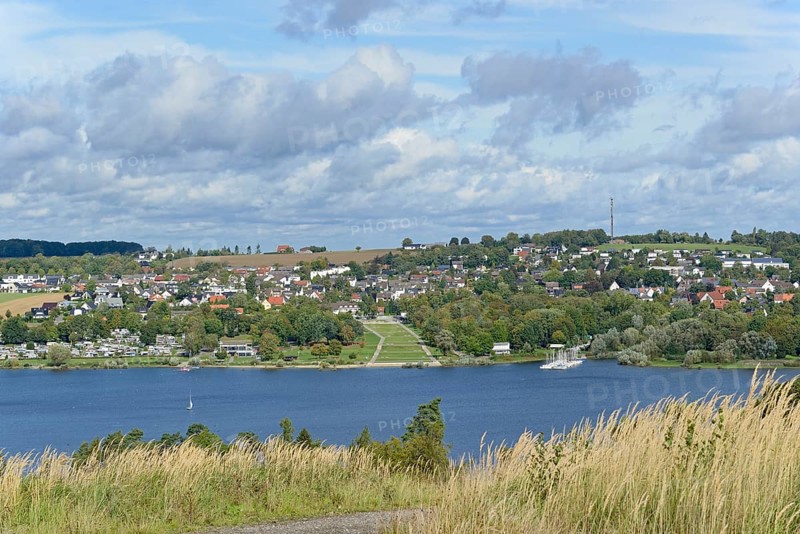 View over the Möhnesee, Körbecke village with the lake park and the lakeside promenade, blue cloudy sky, Möhnetalsperre, North Rhine-Westphalia, Germany