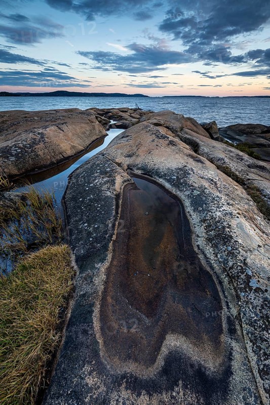 Rocky coastline with water puddles and grass during a sunset-lit evening, Skjeberg, Sarpsborg, Ostfold, Norway