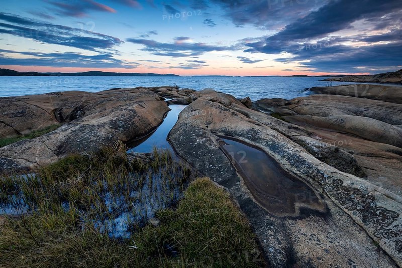 Large rocks with puddles on the coast during a sunset with clouds in the sky, Skjeberg, Sarpsborg, Ostfold, Norway