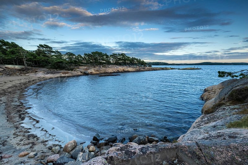 Small bay with sandy beach, surrounded by rocks and pine trees under a partly cloudy sky, Skjeberg, Sarpsborg, Ostfold, Norway