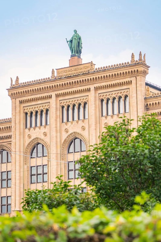 Large historic building with statue on the roof, surrounded by green vegetation, Munich, Germany