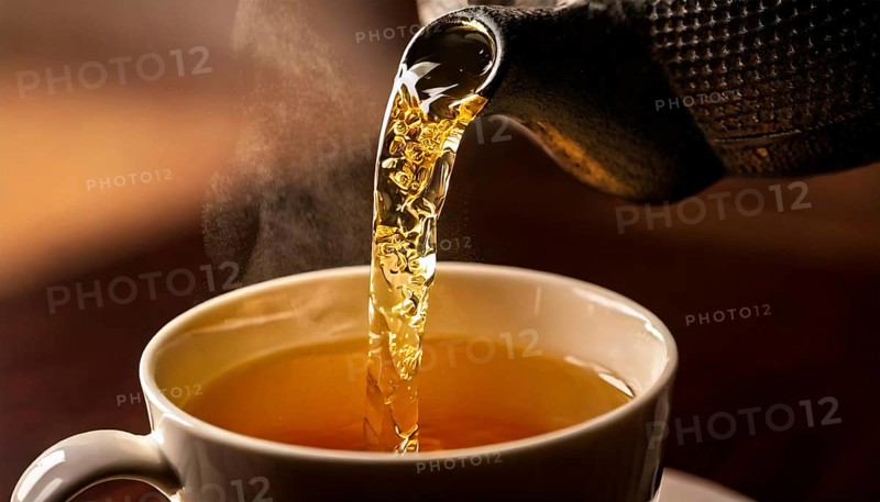AI-generated close-up image showing a teapot from which tea is poured into a cup, AI generated