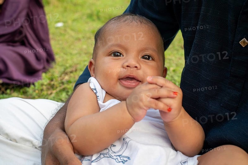 Baby sits on the ground, looking curious in an outdoor setting-Dhaka, Bangladesh