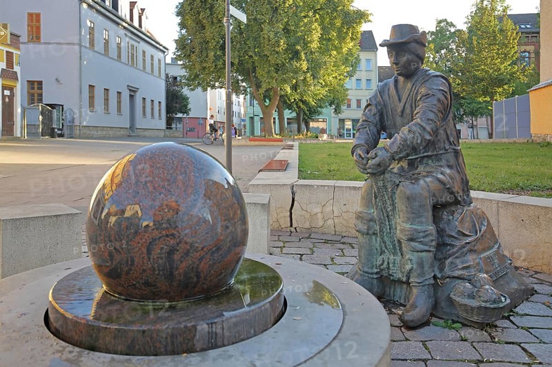 Monument to founder David Strickermann, town history on the development of the textile industry, seated male figure with tub and ball of wool, symbols, wool, ball, bronze sculpture, modern art, rotating granite ball, stone ball, fountain, Strickermannbrunnen, Schulplatz, Apolda, Thuringia, Germany