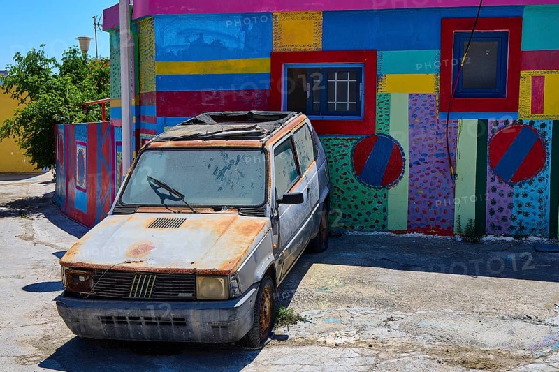 Neglected old car in front of a colourfully painted urban building, Kattavia village, southern tip of Rhodes, Rhodes, Dodecanese, Greek Islands, Greece