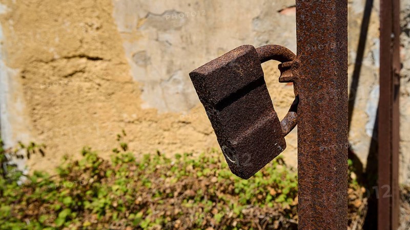 Rusted lock on a metal post in front of a weathered wall with plants in the background, Old silk factory, German Wehrmacht military prison, concentration camp, Lost Place, Kattavia, Rhodes, Dodecanese, Greek Islands, Greece