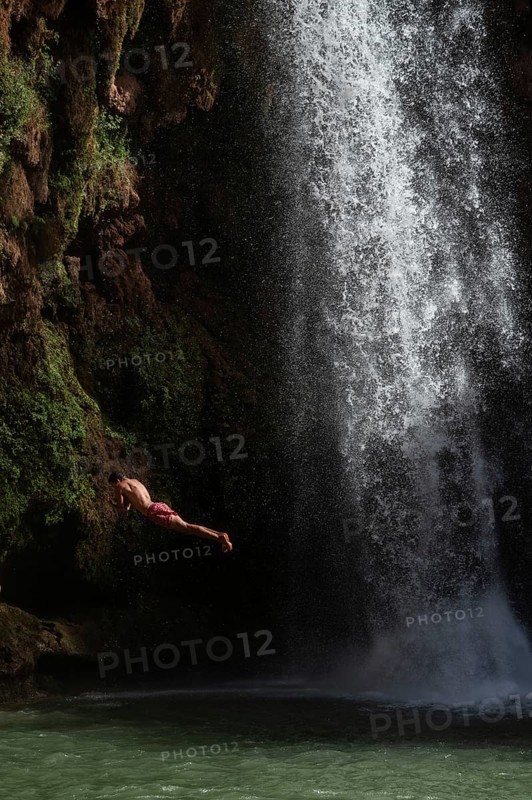 A Moroccan young man jumps from the high rock into the water under a waterfall Ouzoud