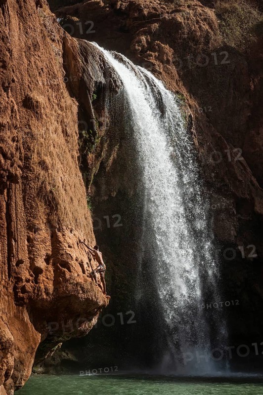 A Moroccan young man climbs the rock before jump from into the water under a waterfall Ouzoud